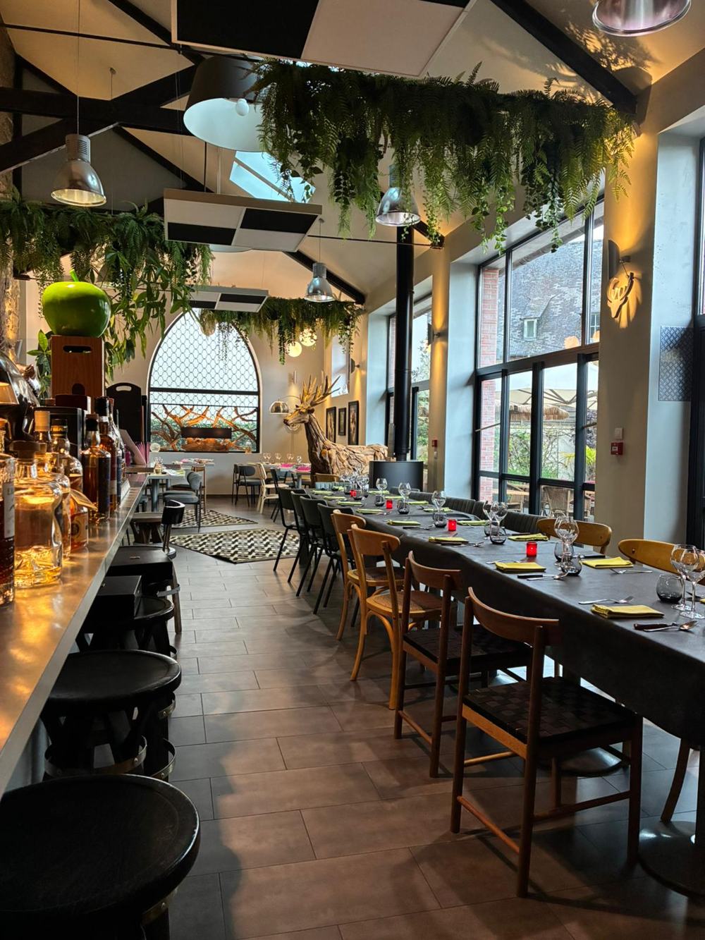 La salle sous la verrière, avec le bar, les grandes tables et les plantes suspendues